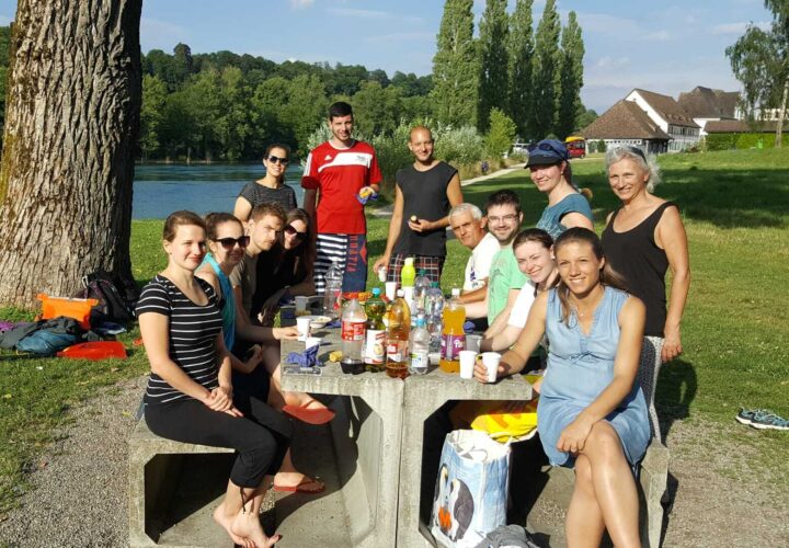 10 Personen um einen Tisch am Rheinufer.