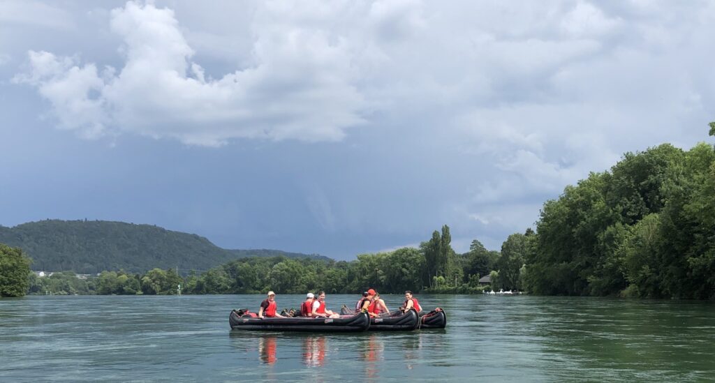 8 Personen in 4 Kanus auf dem Rhein bei bewölktem Himmel.