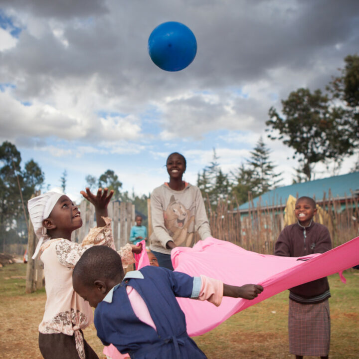 Fünf kenianische Kinder spannen ein pinkiges Tuch und spielen mit einem blauen Ball
