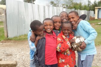 6 lachende kenianische Kinder, die sich umarmen und einen Fussball halten